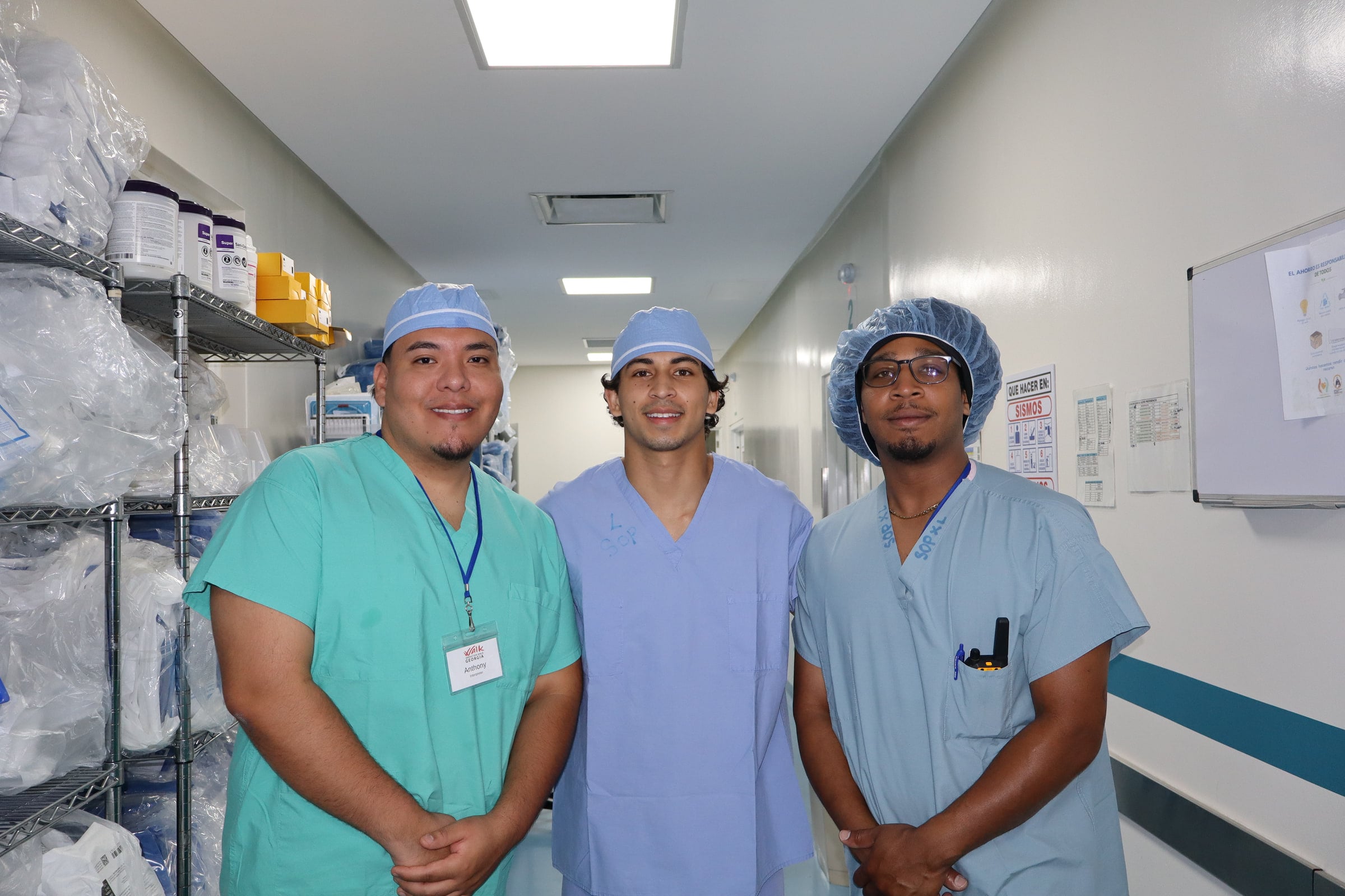 Three clinicians in scrubs smile together in a hospital corridor.