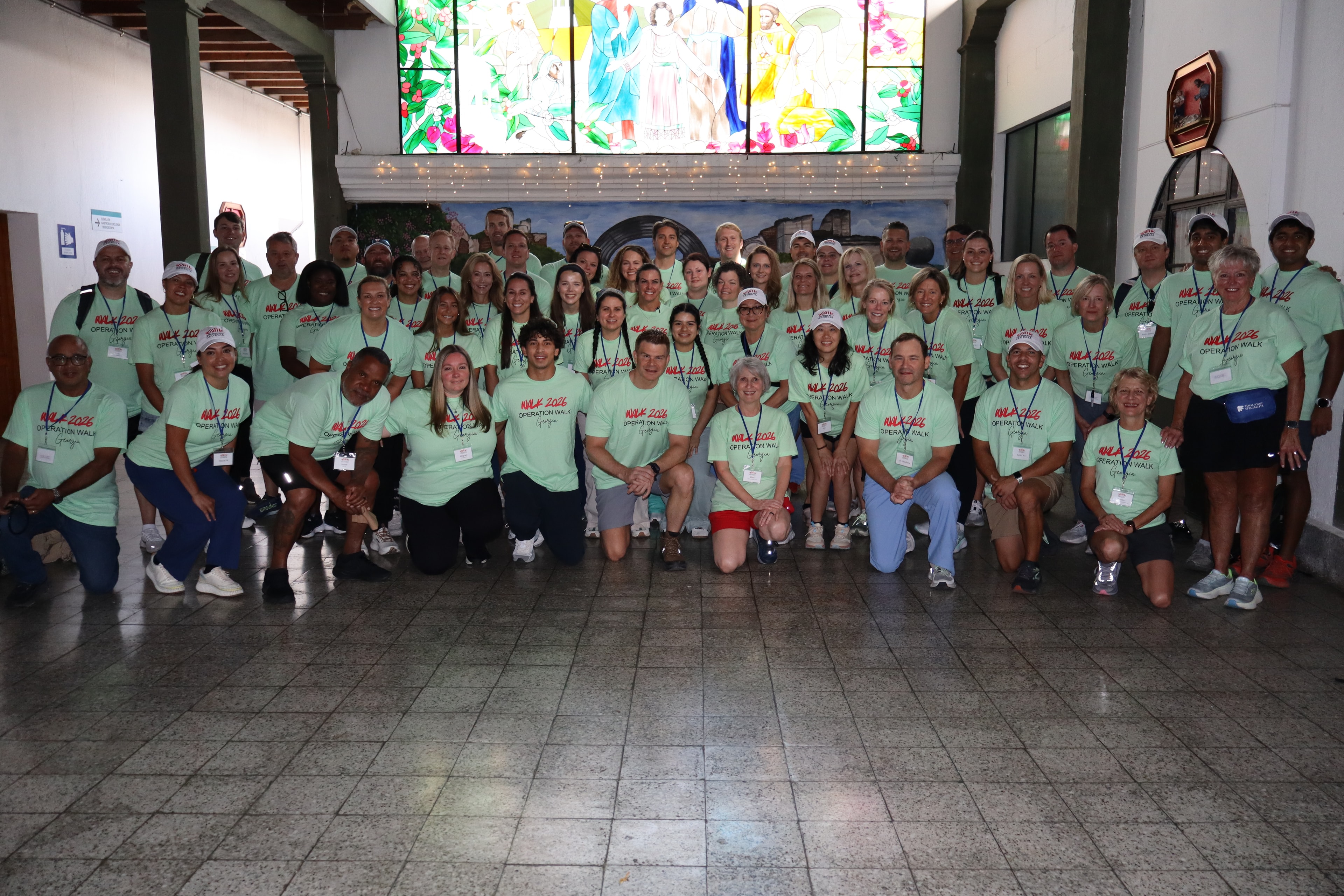 The Operation Walk Georgia team gathers beneath a stained-glass window at Obras.