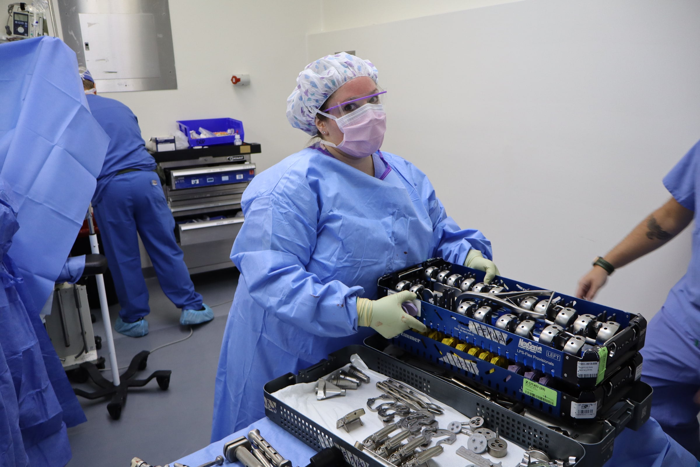 A team member in scrubs arranges surgical instruments on a covered tray.