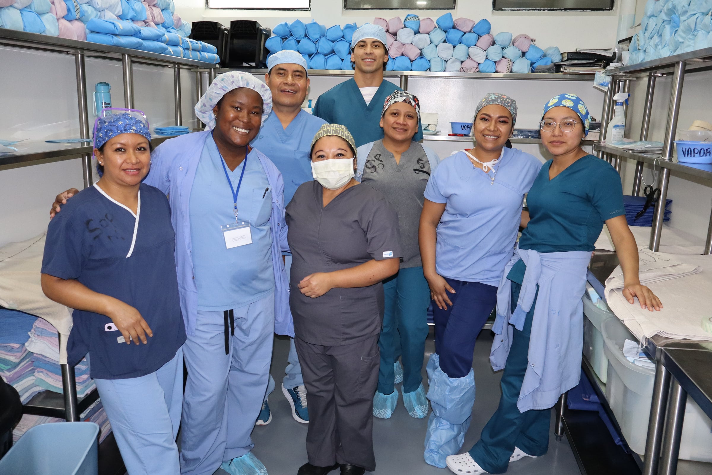 Team members stand together beside shelves of wrapped instrument trays.