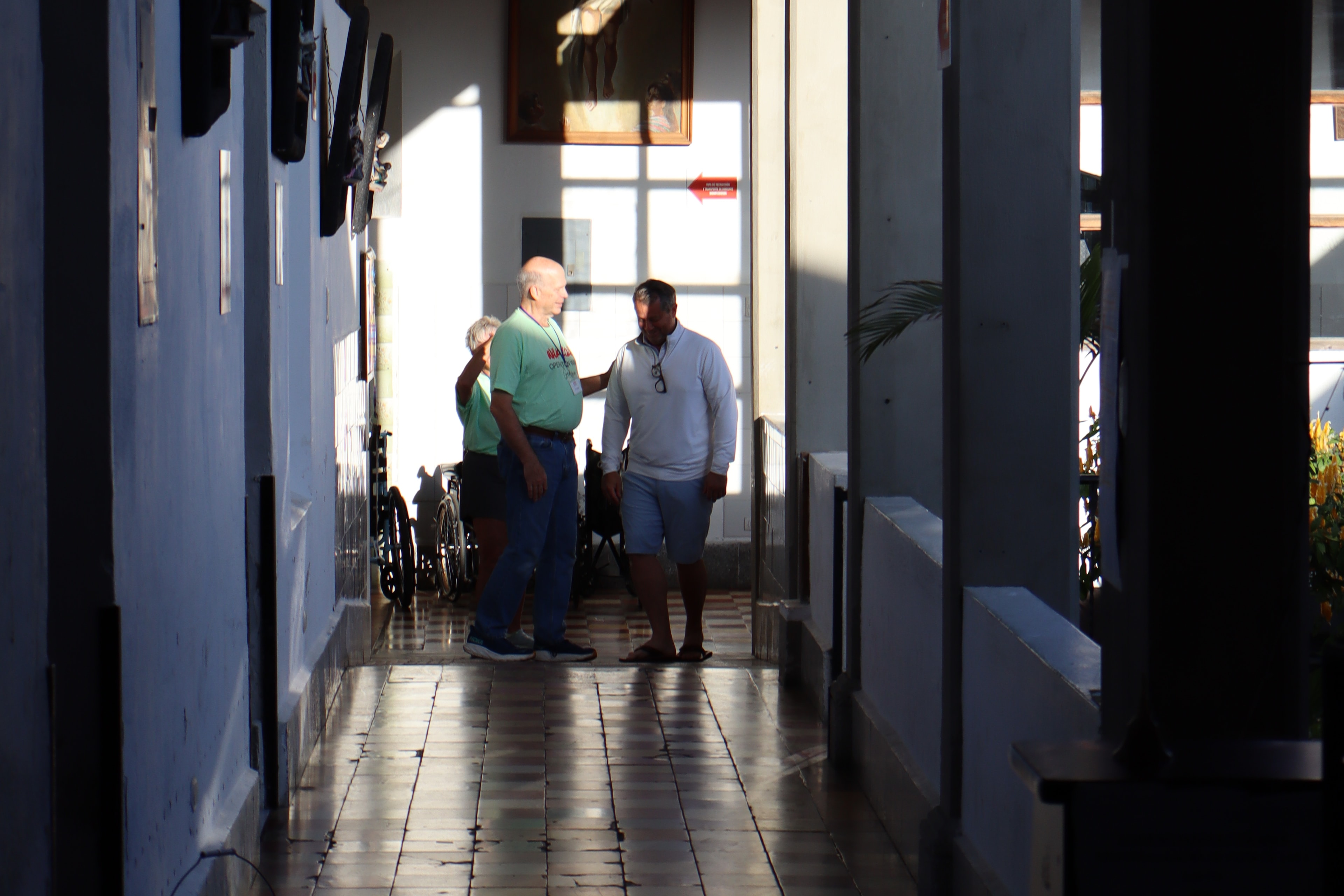 Late light falls along a tiled hospital corridor as team members talk at the far end.