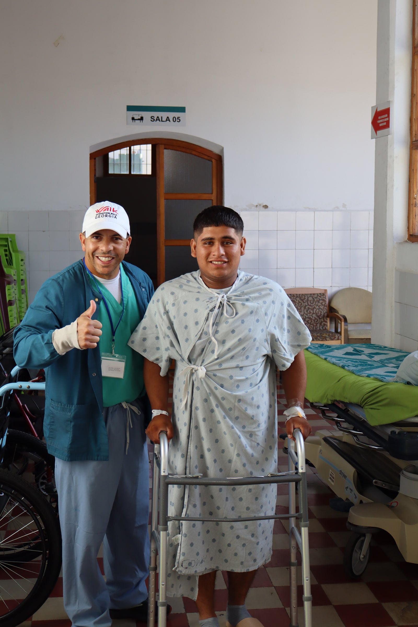 A patient walks the corridor with a walker and gives a thumbs up beside a team member.