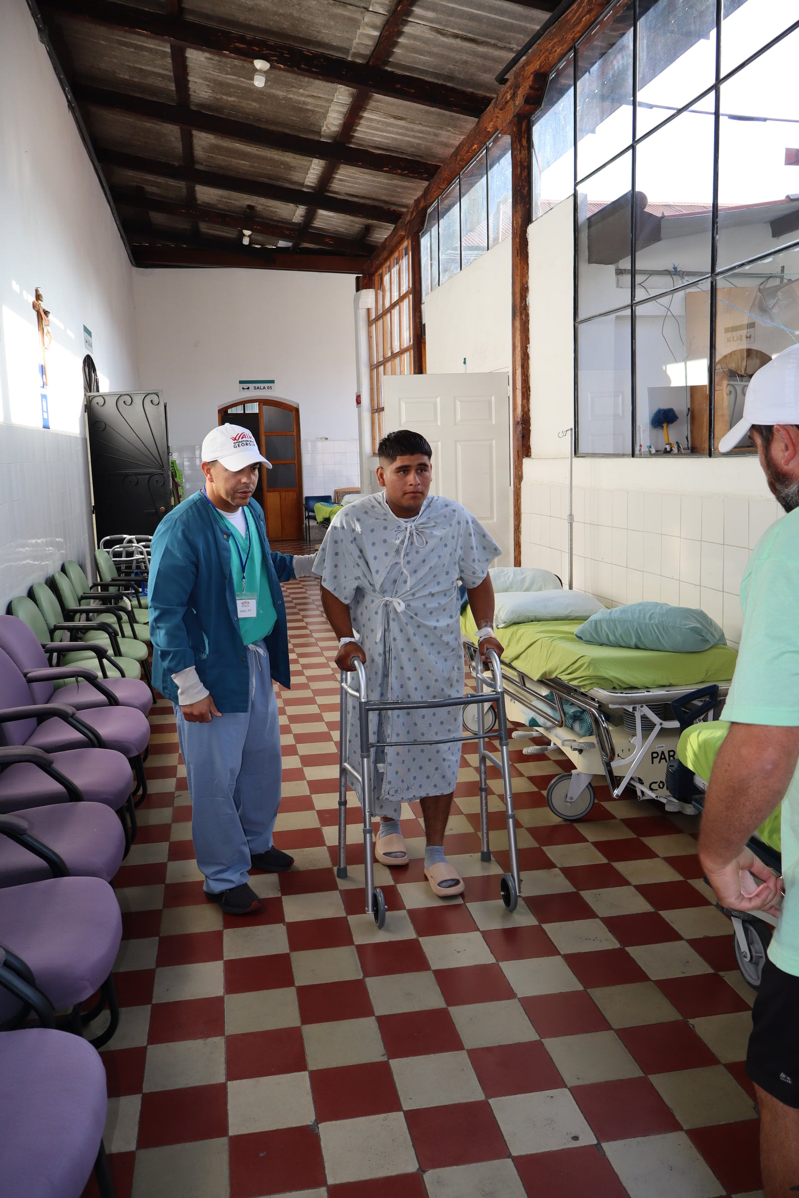 A patient walks down a hospital corridor with a walker as team members follow.